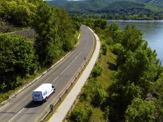Delivery van driving along a mountain road beside a lake.