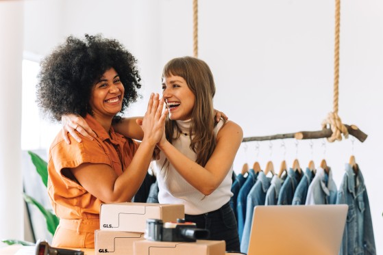 Two women giving each other a high-five while preparing packages in a retail store.
